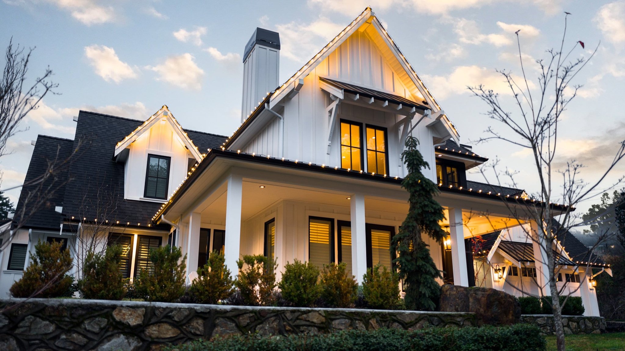 Twilight exterior of a modern farmhouse-style home with string lights and covered porch
