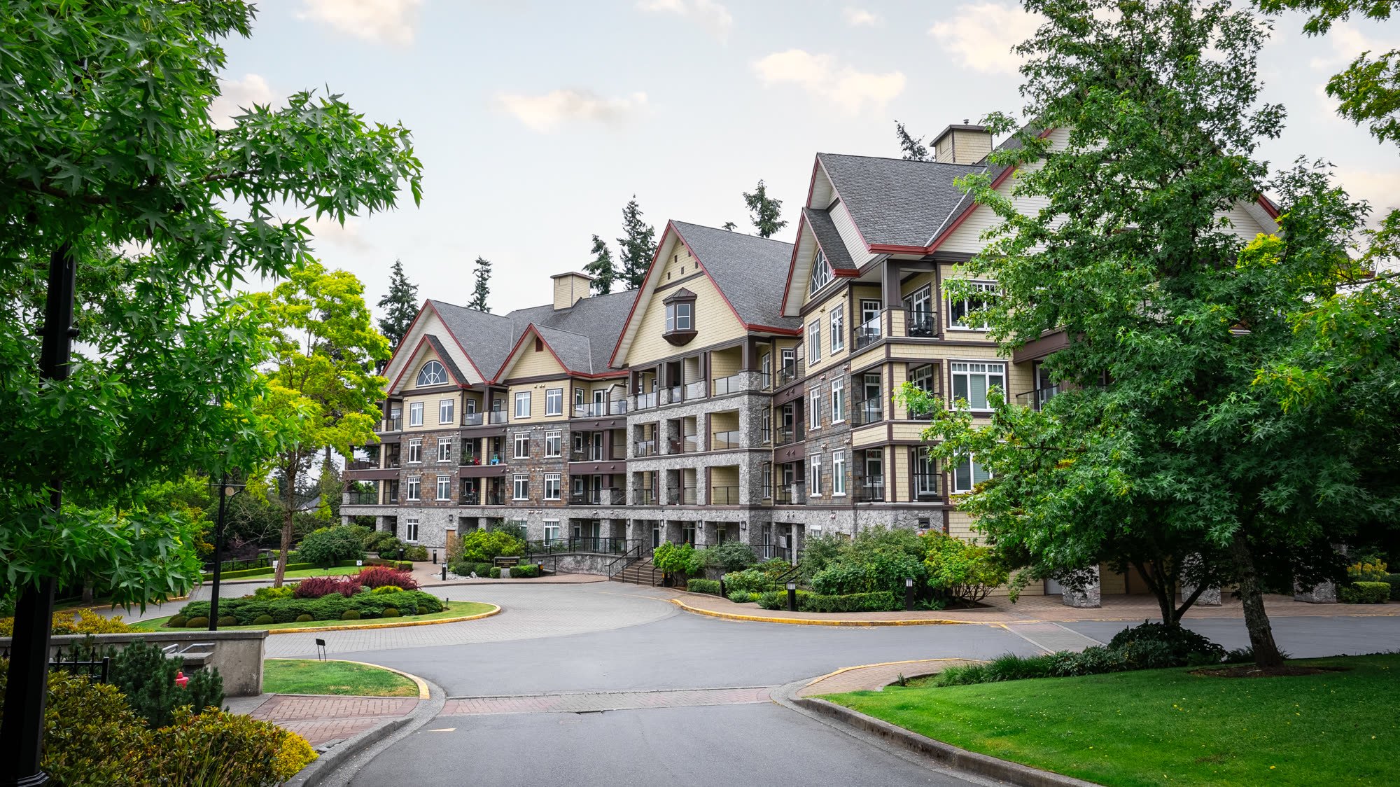 Low-rise condo building with peaked rooflines and mature landscaping