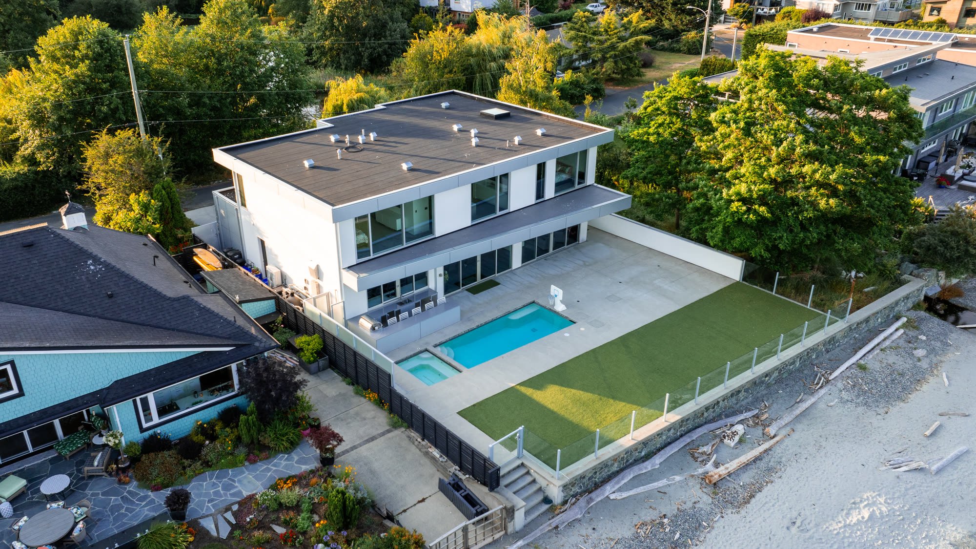 Modern white beachfront home with a pool and turf yard above the shoreline