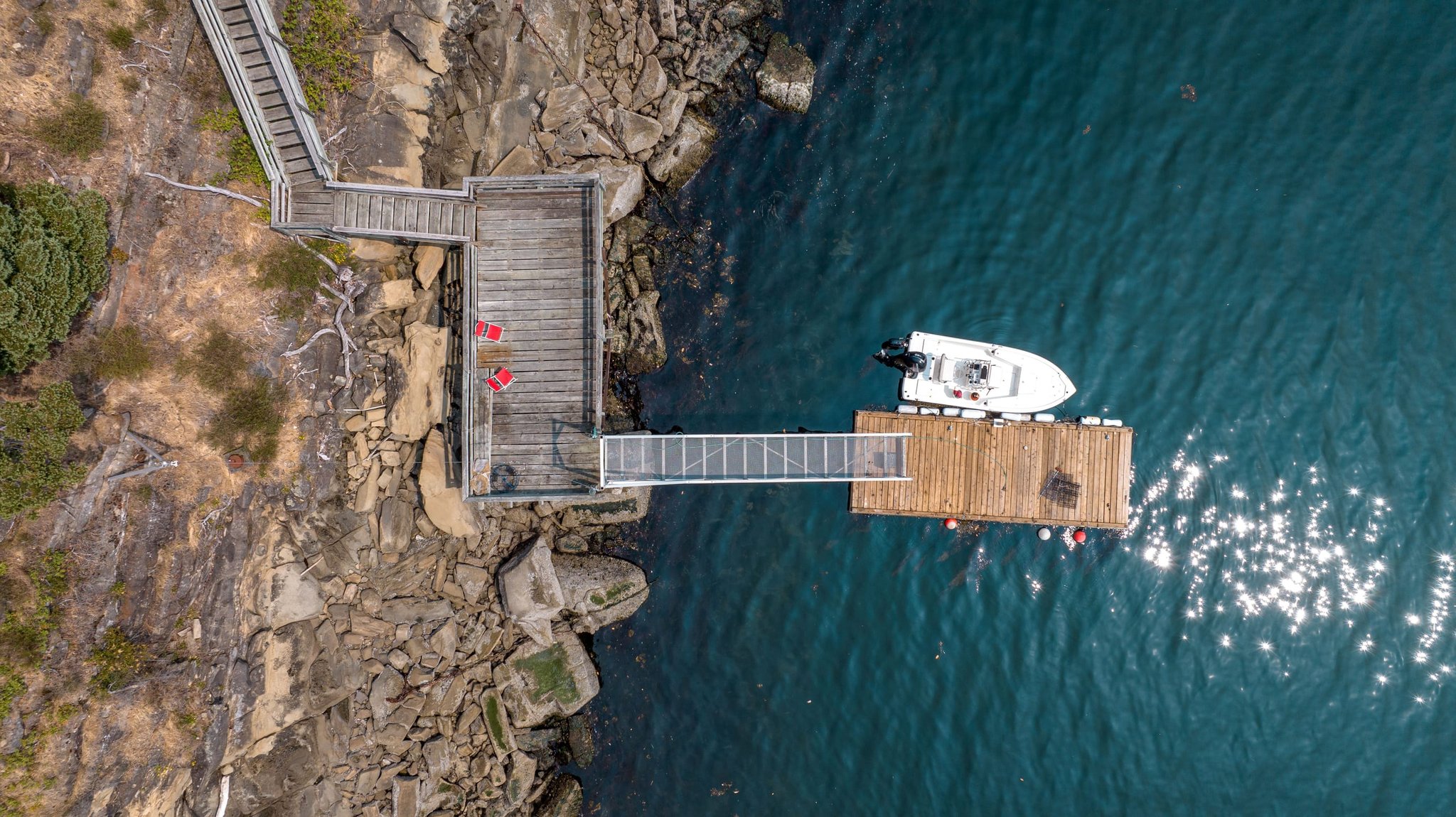 Private dock and moored boat in clear turquoise water below a rocky point