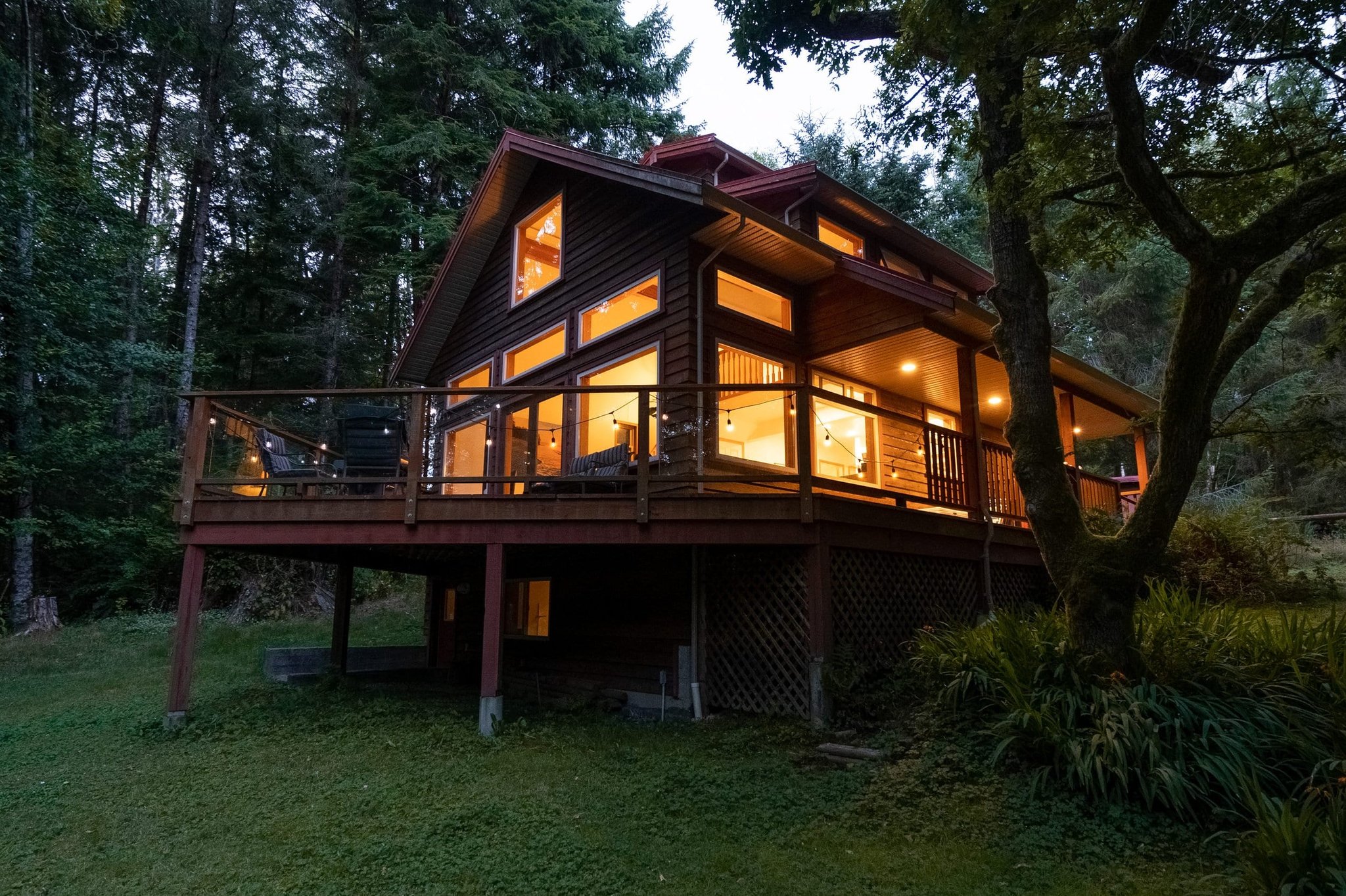 Twilight exterior of a wood-sided home with wraparound deck in the forest